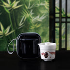 Guppy-pattern porcelain brewer and cup with black zip case before a green bamboo backdrop
