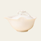 Ivory-white teapot shown straight on against a pale cream background with its spout facing left