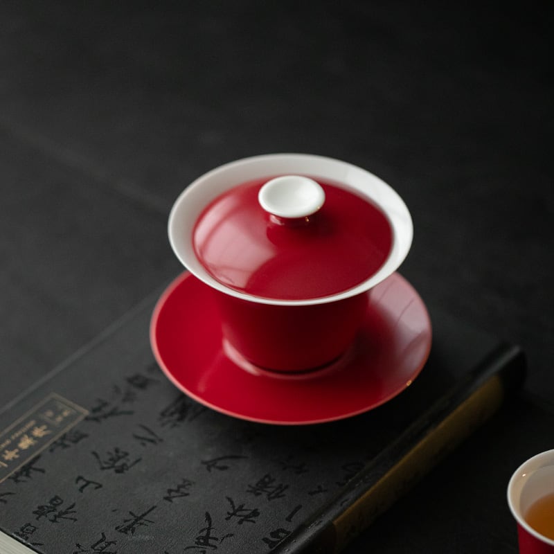 Close view of a red-and-white lidded gaiwan on its matching saucer