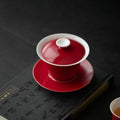 Close view of a red-and-white lidded gaiwan on its matching saucer
