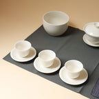 Three white porcelain tea cups on matching saucers with gaiwan and wastewater bowl