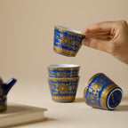 Hand lifting one Qingding Gold Floral Tasting Cup above three arranged cups