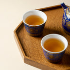 Two Qingding Gold Floral Tasting Cups filled with tea on a wooden tray