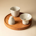 Wood Ash Jinzhao Tea Strainer beside a pitcher and stacked cups on a wooden tray